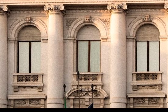 La facciata di un istituto di credito: colonne, finestre ad arco e la bandiera italiana